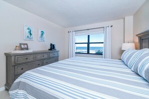A bedroom with a large bed, a dresser, a window with a view of the ocean, and artwork on the wall. - #305 Sandcastle Oceanfront 3/2 Traffic Free Beach Ponce Inlet (Ponce Inlet)