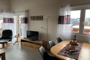 A room with a television, a dining table with chairs, a sofa, and a window with curtains. - Panoramic View - Gallery (Tschiertschen)