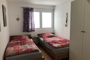 A bedroom with two beds, a window with curtains, a bedside table, and a wardrobe. - Panoramic View - Gallery (Tschiertschen)