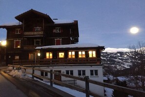 A two-story building with a balcony and a snow-covered roof, situated in a mountainous area. - Panoramic View - Gallery (Tschiertschen)