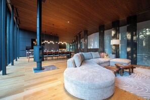 A modern interior with a large sectional sofa, a dining area, and a wood-burning stove.