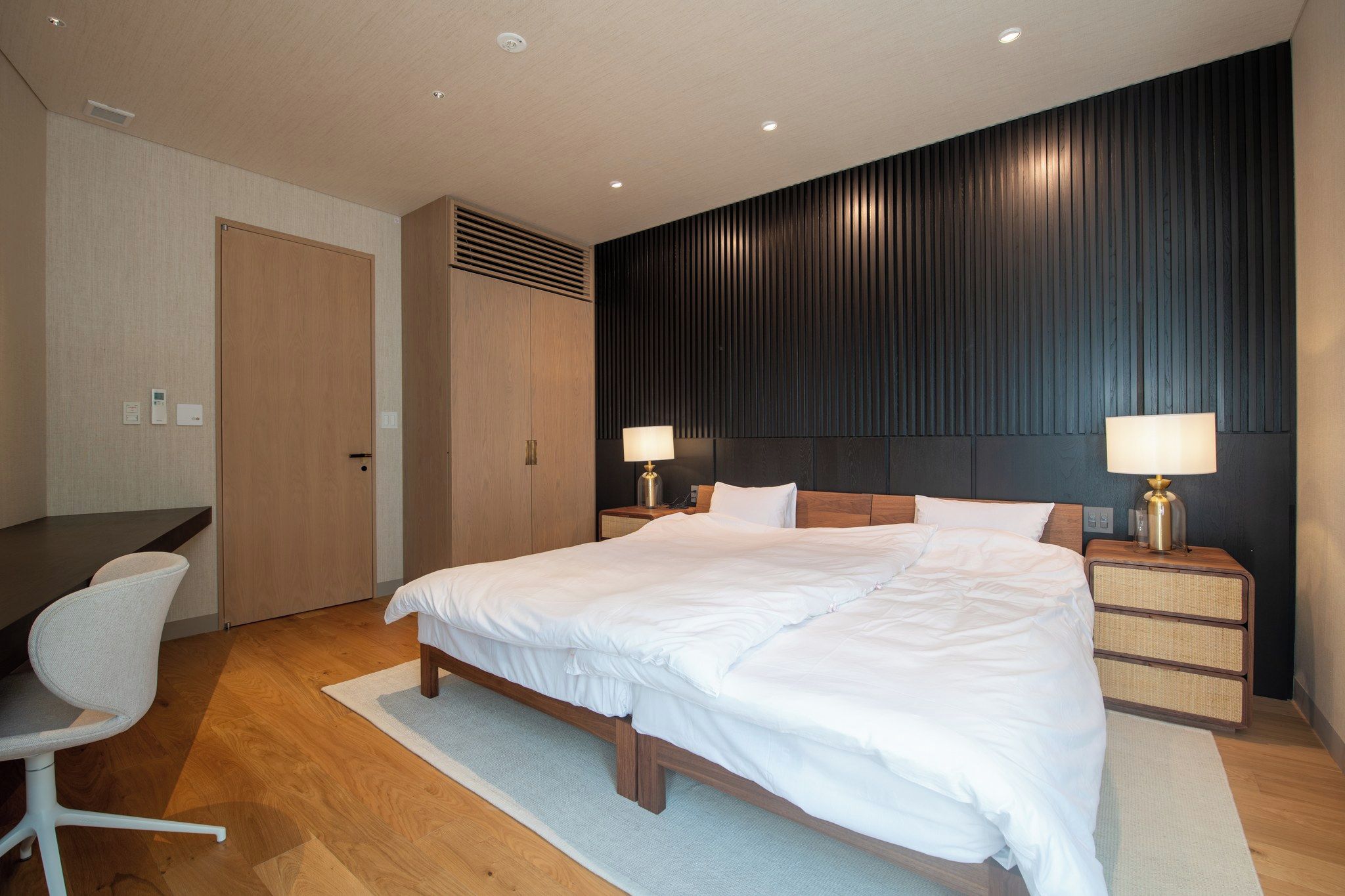 A modern hotel room with a large bed, bedside lamps, a desk, and a chair.