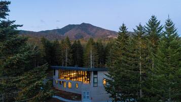 Uma casa moderna rodeada por floresta densa, com uma montanha ao fundo.