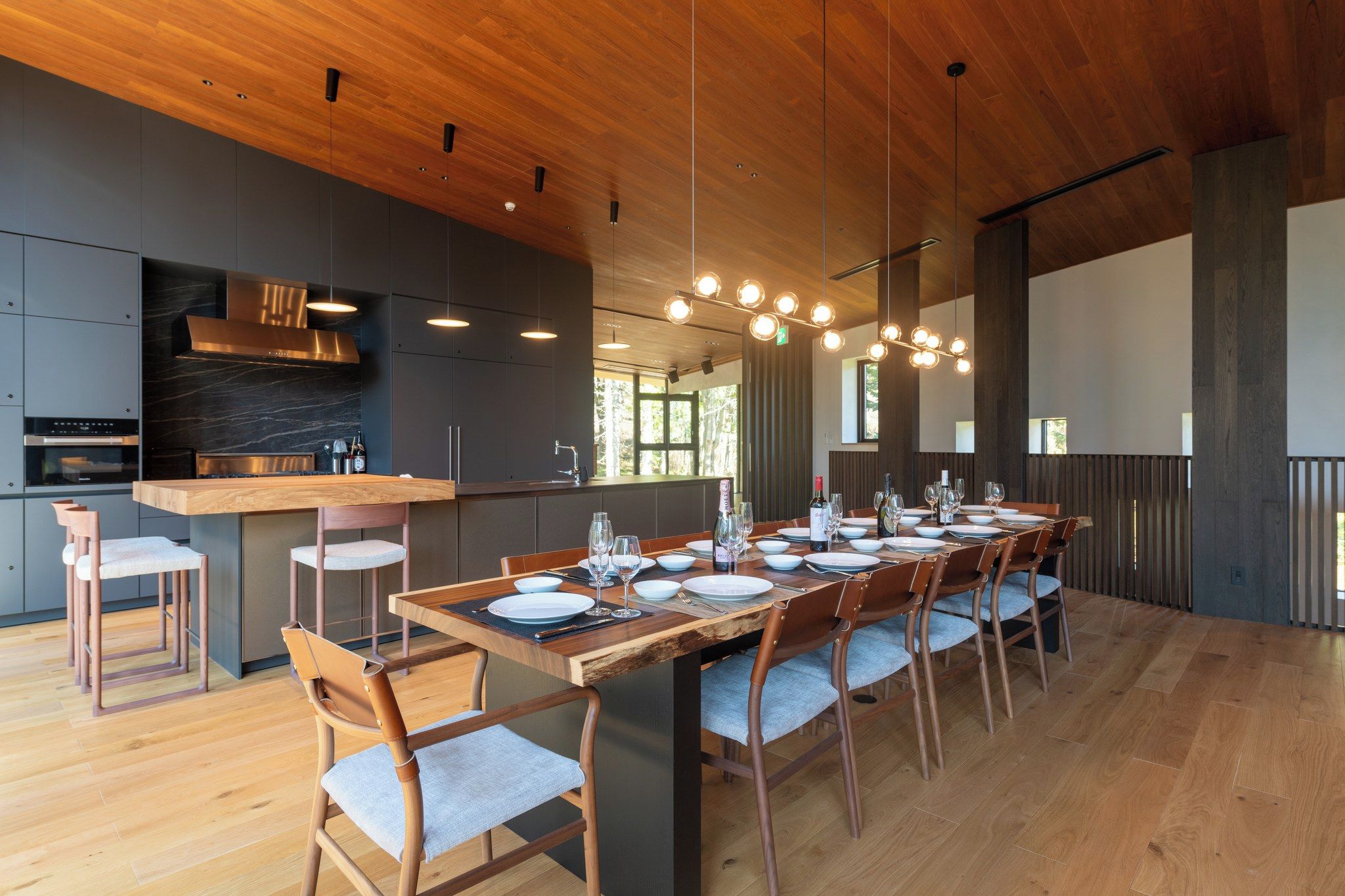 Cozinha moderna com ilha central, área de jantar com mesa comprida posta para seis pessoas, e uma janela grande que oferece luz natural.