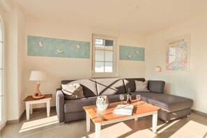 A living room with a grey sofa, a wooden coffee table, a lamp, and a window. - Apartment Große Freiheit (Ostseebad Nienhagen)