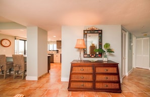 A room with a wooden dresser, a mirror, a lamp, and a dining area with chairs and a table. - #306 Seychelles 2/2 Southeast Corner Oceanfront Condo on Traffic Free Beach (Daytona Beach Shores)