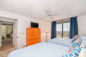 A hotel room with a bed, a wooden dresser, a ceiling fan, and a view of the outside. - #306 Seychelles 2/2 Southeast Corner Oceanfront Condo on Traffic Free Beach (Daytona Beach Shores)