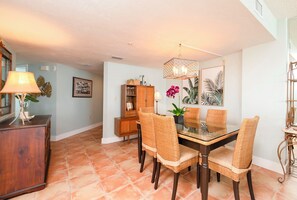 A dining area with a glass-top table, wicker chairs, a wooden cabinet, and a hanging light fixture. - #306 Seychelles 2/2 Southeast Corner Oceanfront Condo on Traffic Free Beach (Daytona Beach Shores)