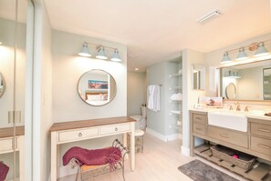 A modern bathroom with a vanity, sink, and mirror. There is a round mirror above the vanity and a rectangular mirror above the sink. The bathroom has a light green wall and a wooden vanity. - #306 Seychelles 2/2 Southeast Corner Oceanfront Condo on Traffic Free Beach (Daytona Beach Shores)