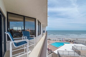Ein Balkon mit zwei Stühlen und ein Poolbereich mit Liegestühlen und einem Pool.