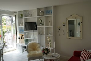 Een woonkamer met een televisie, witte planken, een rode bank en een spiegel.