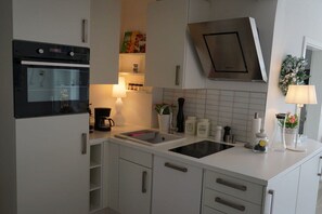 A modern kitchen with white cabinetry, a built-in oven, a stainless steel range hood, and a sink. - Holiday apartment with 1 bedroom (Timmendorfer Strand)