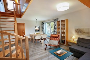 A modern living room with a wooden staircase, a dining area, and a bookshelf. - House by the dike, mill, 1st floor, 60m² (Prerow)
