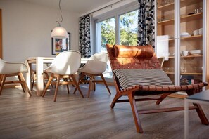 A modern dining area with a wooden table, white chairs, and a leather chair with a striped cushion. - House by the dike, mill, 1st floor, 60m² (Prerow)