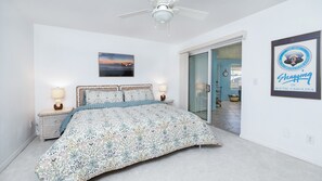 A bedroom with a bed, two bedside lamps, a ceiling fan, a framed picture, and a door leading to a bathroom. - 3202 Towers in Ponce Inlet, FL (Ponce Inlet)