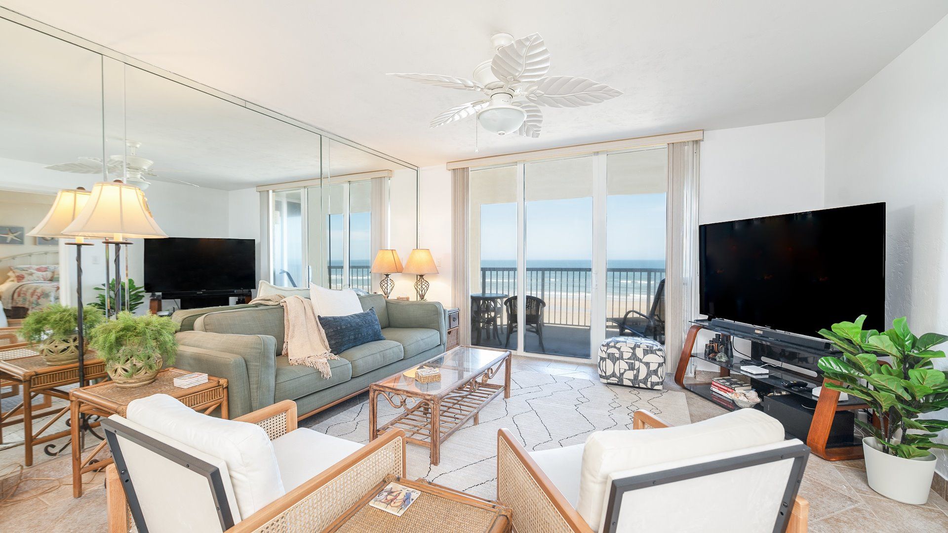 A spacious living room with a large flat-screen TV, comfortable seating, and a balcony with a view.