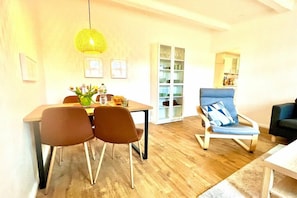 Ein Essbereich mit einem Holztisch, braunen Stühlen, einer gelben Pendelleuchte und einem blauen Sessel mit Kissen.