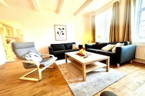 A modern living room with a sofa set, a coffee table, and a chair. There is a framed artwork on the wall and a window with curtains. - Holiday apartment with 1 bedroom (Fehmarn OT Klausdorf)