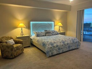 A bedroom with a large bed, two bedside tables with lamps, a chair, and a view of the outdoors through a sliding door. - 3307 Harbor Village in Ponce Inlet, FL (Ponce Inlet)