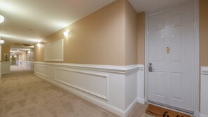 A hallway with a carpeted floor, a white door with a keyhole, and a wall-mounted light fixture. - 3307 Harbor Village in Ponce Inlet, FL (Ponce Inlet)