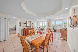 A spacious dining area with a wooden table and chairs, a kitchen in the background, and large windows offering a view of the outside. - 3307 Harbor Village in Ponce Inlet, FL (Ponce Inlet)