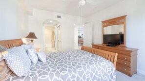 Une chambre à coucher comprenant un lit, une commode, un téléviseur et un ventilateur de plafond.