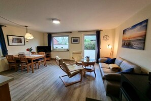 Ein Wohnzimmer mit einer Couch, einem Esstisch mit Stühlen, einem Fernseher und einem Bild an der Wand.