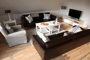A living room with a black leather sofa, a white armchair, a coffee table, a TV on a stand, and a lamp on a side table. - Holiday apartment with 2 bedrooms (Timmendorfer Strand)