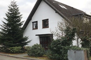 A white building with a gabled roof, two windows, and a dark door. - Holiday apartment with 2 bedrooms (Timmendorfer Strand)