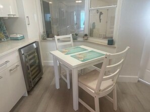 A dining area with a white table and chairs, a refrigerator, and a window with a view of the interior. - 3602 Towers in Ponce Inlet, FL (Ponce Inlet)