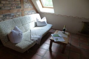 A room with a sofa, a table with a bottle and papers, a window, and a brick wall. - at the gateway to Fischland (Ribnitz-Damgarten)