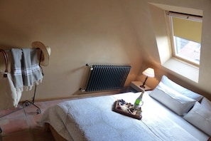 Et soveværelse med seng, radiator, et vindue og et natbord med lampe.
