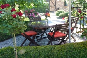 An outdoor seating area with a round table and chairs, surrounded by lush greenery and flowering plants. - at the gateway to Fischland (Ribnitz-Damgarten)