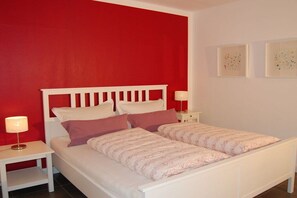 A single-bed room with a white headboard, two bedside tables with lamps, and a red accent wall. - Buchholzer Steinbachtal (Buchholz)