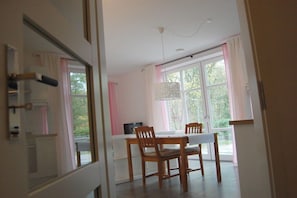 A dining area with a table and chairs, a hanging light fixture, and a view through the window. - Buchholzer Steinbachtal (Buchholz)