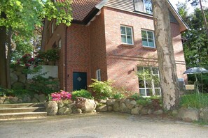 A brick house with a stone wall, a blue door, and a small garden with pink flowers. - Buchholzer Steinbachtal (Buchholz)