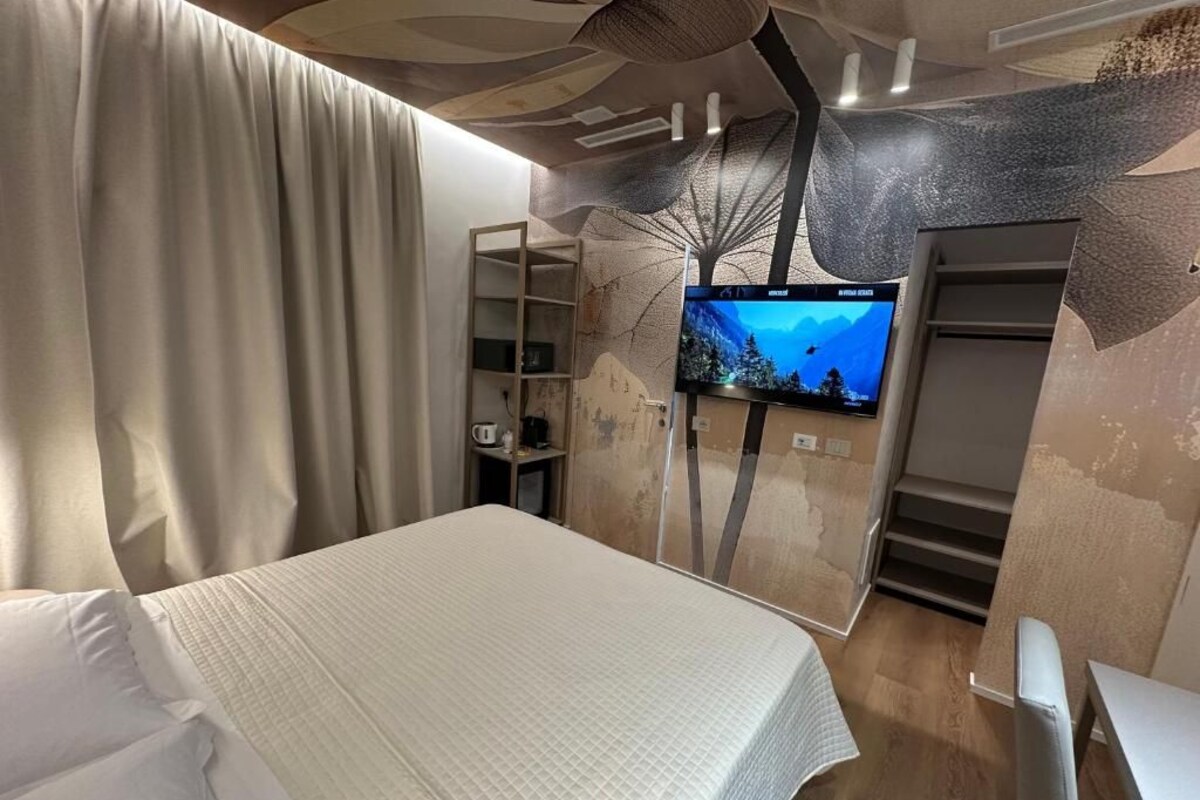 Une chambre d’hôtel avec un lit, une télévision et un mur décoré d’un motif représentant un arbre.
