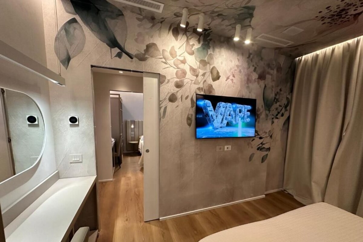 Une chambre à coucher avec un lit, un téléviseur fixé au mur et une porte donnant sur une autre pièce.