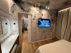Une chambre à coucher avec un lit, un téléviseur fixé au mur et une porte donnant sur une autre pièce.
