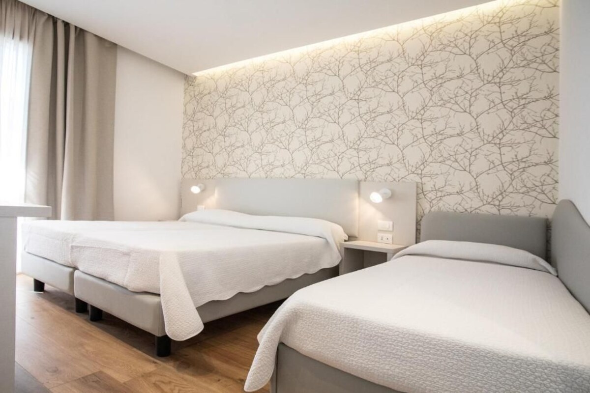 Une chambre d’hôtel avec deux lits, une table de chevet et un mur décoré d’un motif représentant une branche d’arbre.