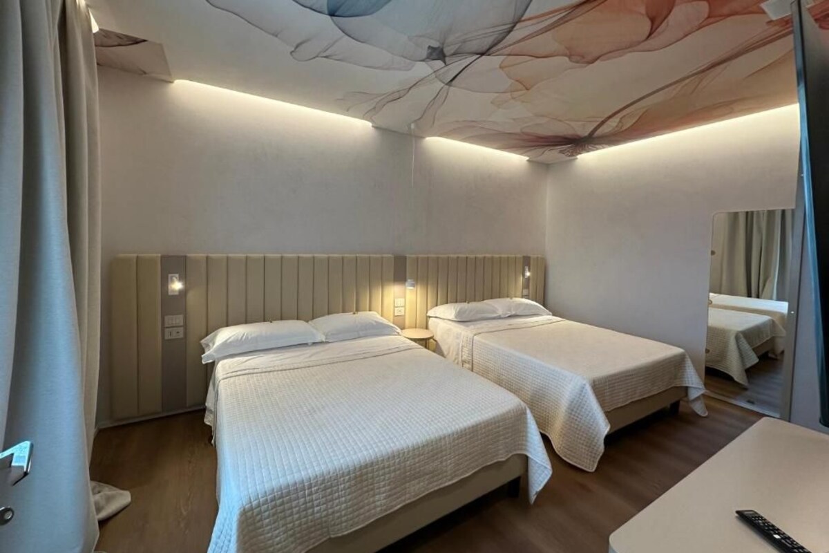 Une chambre d’hôtel avec deux lits, un bureau et un plafond au design original.