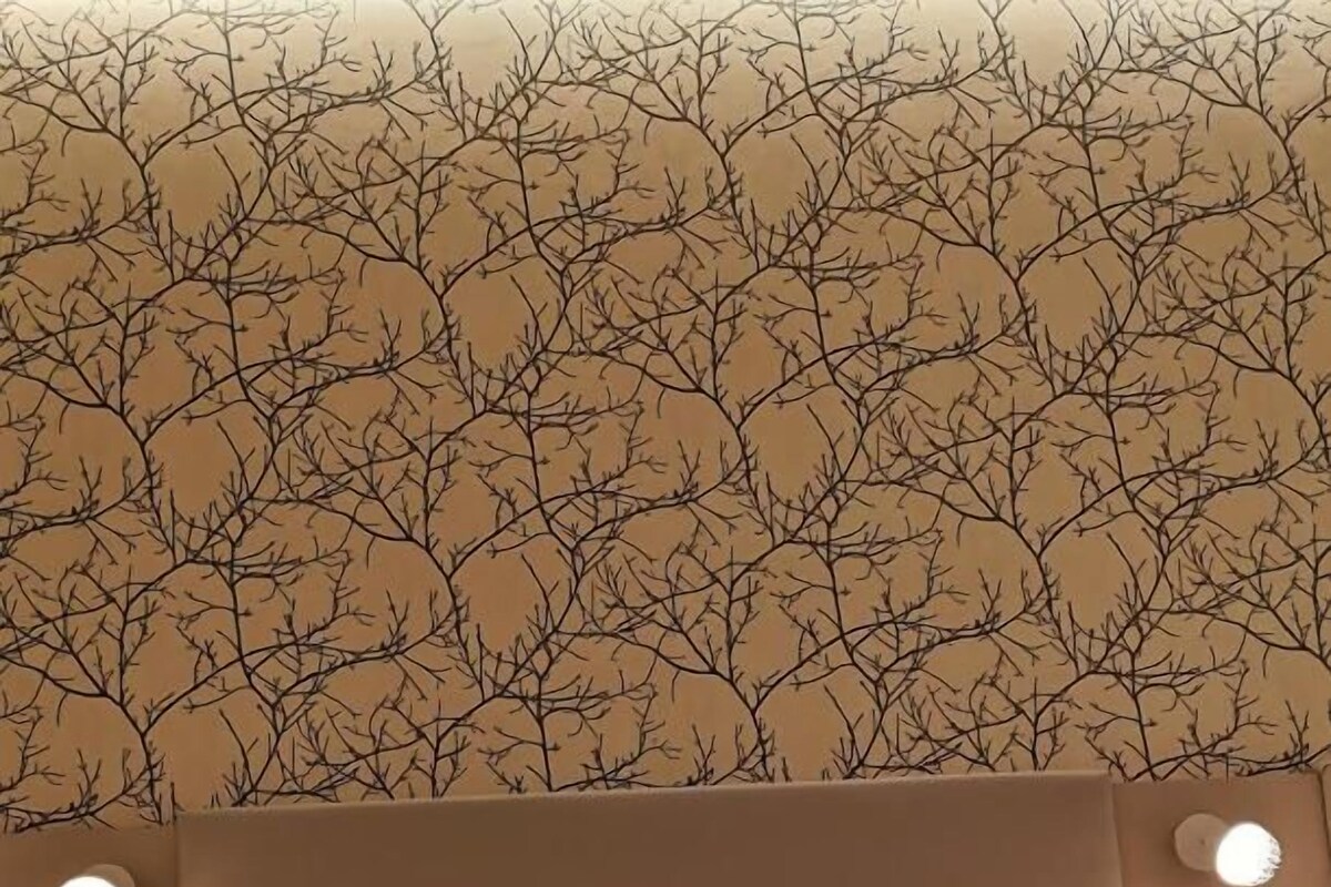 Une chambre d’hôtel avec un lit, une tête de lit et un mur orné d’un motif d’arbre. On y trouve deux interrupteurs fixés au mur et un luminaire rond.