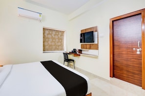 Quarto de hotel com cama, escrivaninha com computador, cadeira, guarda-roupa e ar condicionado.