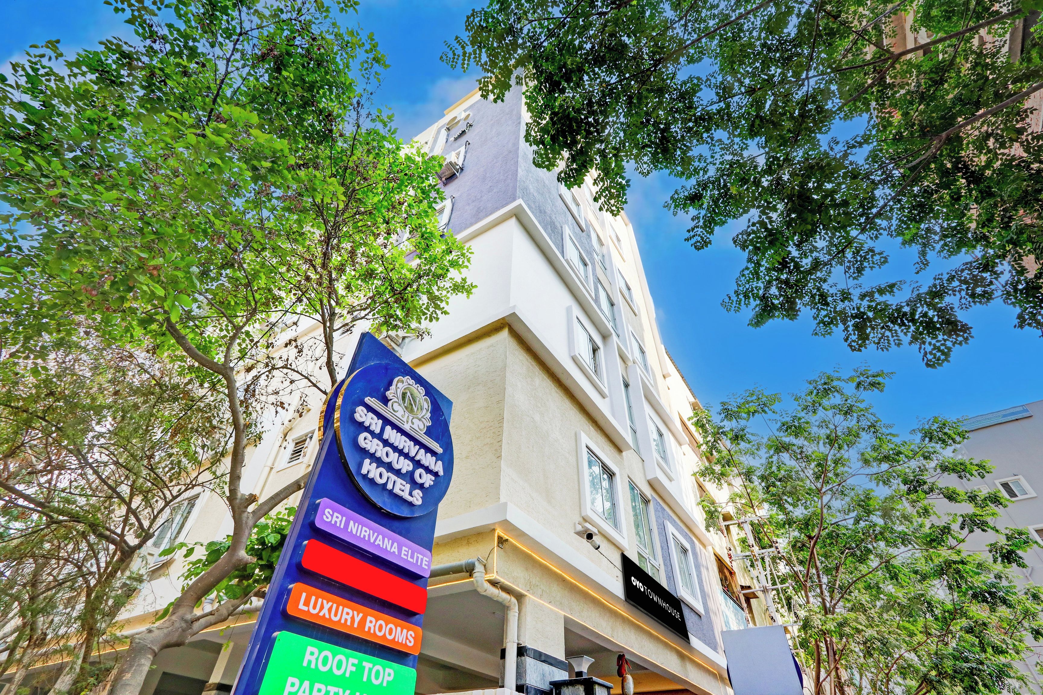 Ein Hotelschild mit verschiedenen Zimmerkategorien, darunter 'NIRVANA GROUP OF HOTELS', 'ELITE', 'LUXURY ROOMS' und 'ROOF TOP PARTY'.