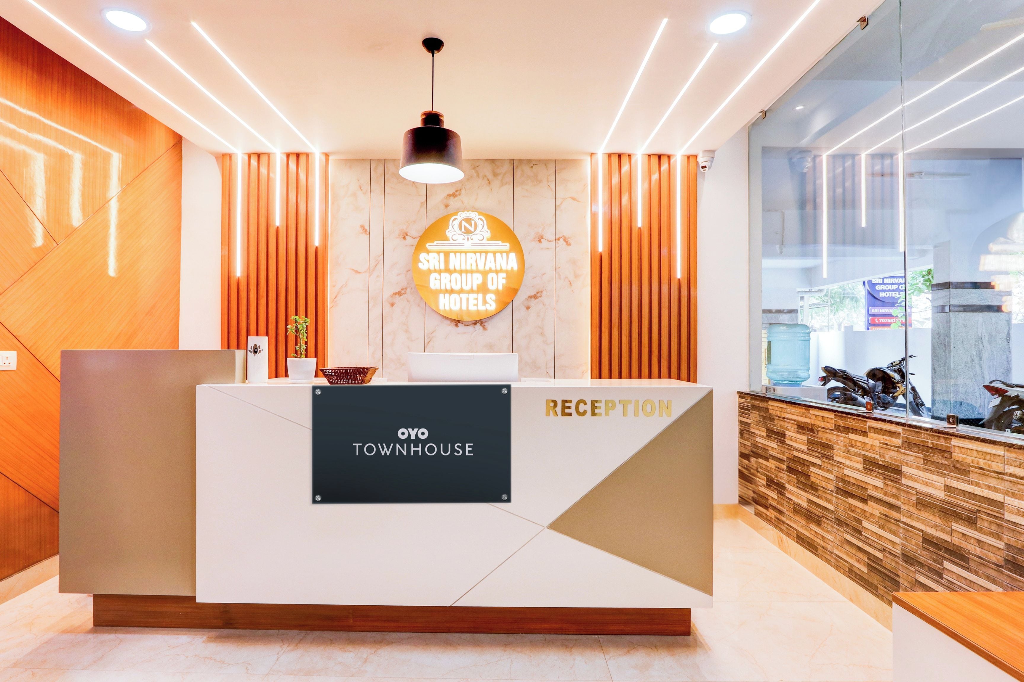 Ein Empfangsschalter mit einem Schild für 'Sri Nirvana Group of Hotels' und 'Oyo Townhouse' in einer modernen Hotelhalle.