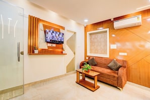 Uma sala de estar moderna com porta de vidro, televisão na parede, painel de parede de madeira, sofá marrom com almofadas e uma pequena mesa com uma planta.