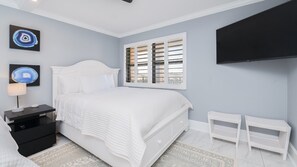A bedroom with a bed, bedside tables, a TV, and artwork on the walls. - 404 Lighthouse Shores (Ponce Inlet)