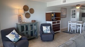 A living room with two armchairs, a sofa, a cabinet with glass doors, a dining table with chairs, and a ceiling fan. - #405 Sandcastle 2/2 Oceanfront Condo Traffic Free Beach (Ponce Inlet)