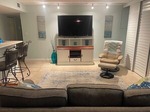 A living room with a flat-screen TV, a sofa, a chair, a dining table with chairs, and a cabinet. - #405 Sandcastle 2/2 Oceanfront Condo Traffic Free Beach (Ponce Inlet)