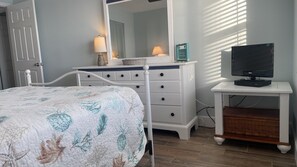A bedroom with a bed, dresser, mirror, television, and a window with blinds. - #405 Sandcastle 2/2 Oceanfront Condo Traffic Free Beach (Ponce Inlet)